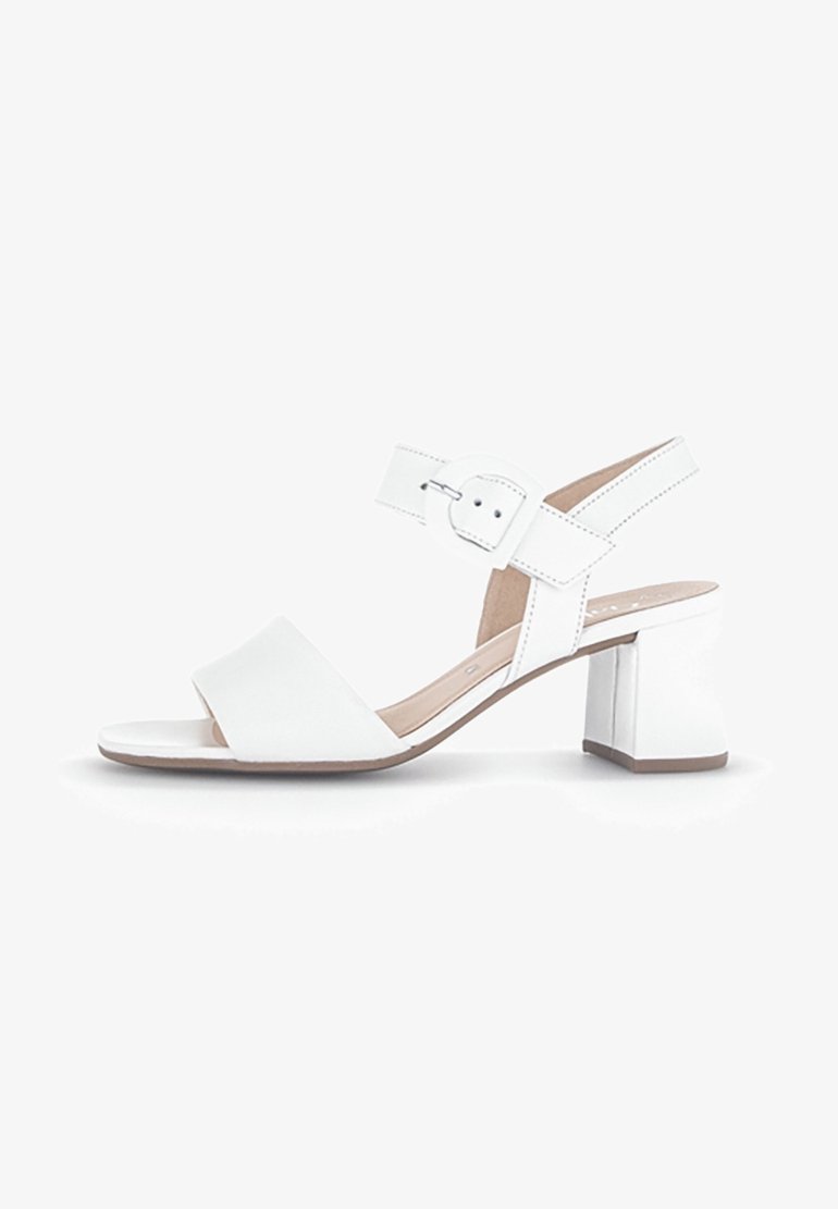 Sandale blanche à bout ouvert avec un talon carré et une sangle de cheville réglable ornée d'une boucle ronde sur fond blanc.