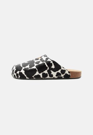 Mule à enfiler avec dessus imprimé vache noir et blanc et semelle en liège, talon plat, profil latéral sur fond uni.