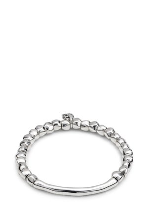 Pulsera de cuentas plateadas con cuentas de forma irregular y un adorno de barra curva y lisa, dispuestas en forma circular sobre fondo blanco.