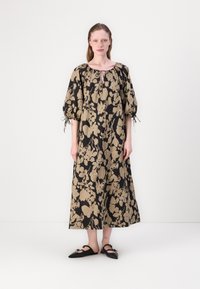 Robe à motif floral noir et beige avec manches bouffantes, décolleté en trou de serrure et coupe décontractée. Associée à des chaussures plates noires.