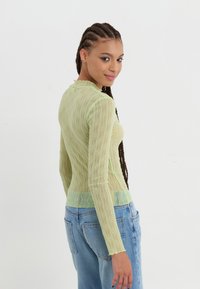 Lys grøn gjennomsiktig langermet topp med bølgete tekstur og bølgete halslinning. Kombinert med høy midje blå denim jeans.