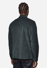 Männer Cordjacke in Dunkelgrün mit klassischem Kragen, langen Ärmeln und geradem Saum. Strukturierter Stoff mit dezenten Rillen.