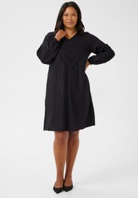 Vestido negro con escote en V, mangas largas abullonadas y detalles de encaje decorativos en el pecho. Silueta en A, corte a la altura de la rodilla.