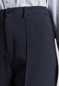 Marinblå byxor med en slät tyg, figurpassande design, sidofickor och en enda knappstängning vid midjan.