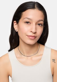 Zilveren metalen chokerketting met een glad, gebogen ontwerp. Het model draagt bijpassende studs. Beige tanktop van een gemêleerde stof.