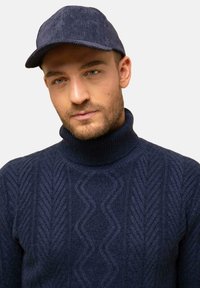 Marineblaue, kabelgezopfte Rollkragenpullover mit strukturiertem Muster; kombiniert mit einer marineblauen Cord-Basecap. Glatte Stoffoberfläche, figurbetonter Schnitt.