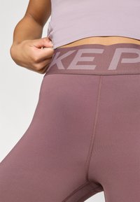 Las mallas moradas cuentan con una cinturilla alta con la marca "Nike Pro". Están hechas de un tejido suave y elástico con costuras planas para mayor comodidad.