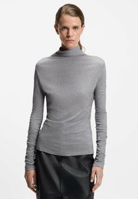 Grijze langwerpige turtleneck top, gemaakt van zachte stof met een aangesloten silhouet, gecombineerd met een zwarte leren rok met een gladde textuur.