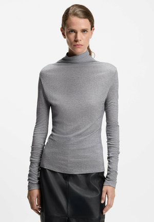 Graues langärmeliges Turtleneck-Oberteil aus weichem Stoff mit taillierter Silhouette, kombiniert mit einem schwarzen Lederrock mit glatter Textur.