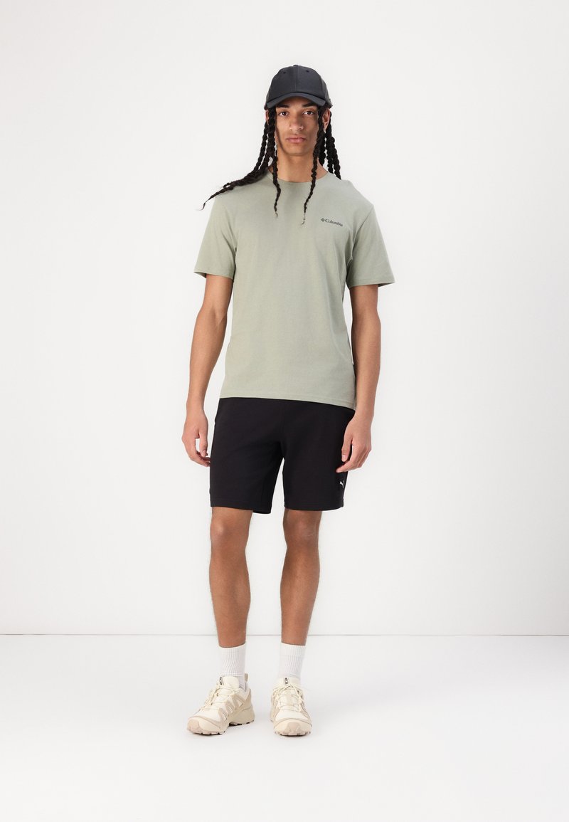 Camiseta corta de manga verde claro con logo, pantalones cortos deportivos negros y zapatillas beige. Incluye una gorra negra y calcetines blancos hasta el tobillo.