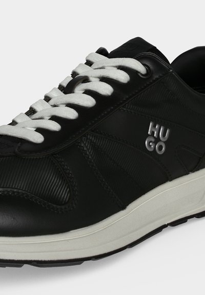Baskets en cuir noir avec lacets blancs et semelle blanche, panneaux latéraux texturés et logo "HUGO" sur le côté extérieur.