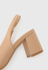 Beige blokhak schoenen met een slingback ontwerp. Glad faux leer materiaal, vierkante neus en gedetailleerde geprofileerde binnenzool.