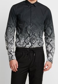 Black long-sleeve shirt with a snake print pattern transitioning from black to white. Features a button-down collar and slim fit. Paired with black pants.