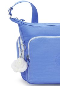 Blå nylonväska med texturerad yta, med vit kant, framficka och ett fluffigt vitt tillbehör fäst vid en silverkedja.