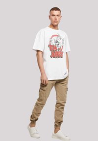 Hvid t-shirt med "Tom and Jerry" grafik, parret med lysebeige cargo-bukser. Modellen har hvide sneakers på; afslappet pasform og korte ærmer.