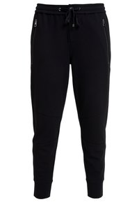 Pantalones de chándal negros confeccionados en una tela suave, con cintura ajustable mediante cordón, bolsillos laterales con cremallera y puños acanalados con detalles de panel.