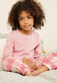 Lichtroze langemouwtop gecombineerd met roze en witte geruite pyjamabroek met kleine blauwe accenten. Getextureerd katoenmateriaal.