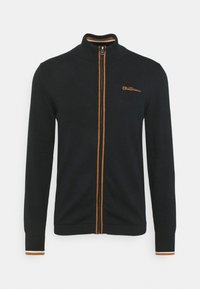 Musta vetoketjullinen takkki oranssein yksityiskohdin ja logolla. Mukana ribbineuloskaulus ja -hihansuut. Sileä kangas ja istuva malli.