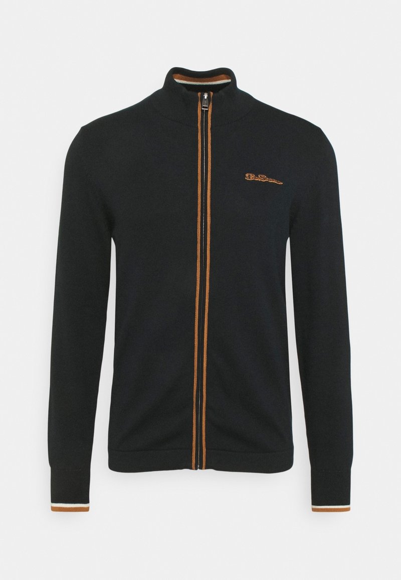 Musta vetoketjullinen takkki oranssein yksityiskohdin ja logolla. Mukana ribbineuloskaulus ja -hihansuut. Sileä kangas ja istuva malli.