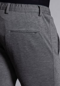 Grå träningsbyxor med en strukturerad tyg, elastisk midja och en platt bakficka. Designen har en strömlinjeformad, åtsittande form.