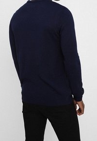 Pull en tricot bleu marine avec un col rond et des poignets côtelés, présentant une texture uni et une coupe ajustée. Vue de dos affichée.