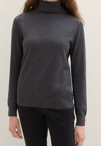 Dunkelgrauer Rollkragenpullover aus weichem Material, körpernahe Passform, lange Ärmel, gerippte Bündchen und Saum, kombiniert mit dunklen Hosen vor einem neutralen Hintergrund.