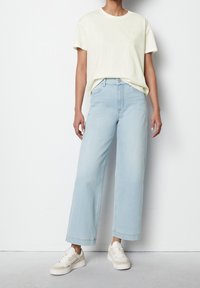 Světle žluté tričko s krátkým rukávem, sladěné s vysokými světle modrými širokými džíny a bílými teniskami s béžovými akcenty.