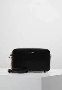 Czarna prostokątna torba na ramię wykonana z teksturowanego materiału, z złotym logo, łańcuszkiem i skórzanym paskiem oraz zamkiem błyskawicznym.