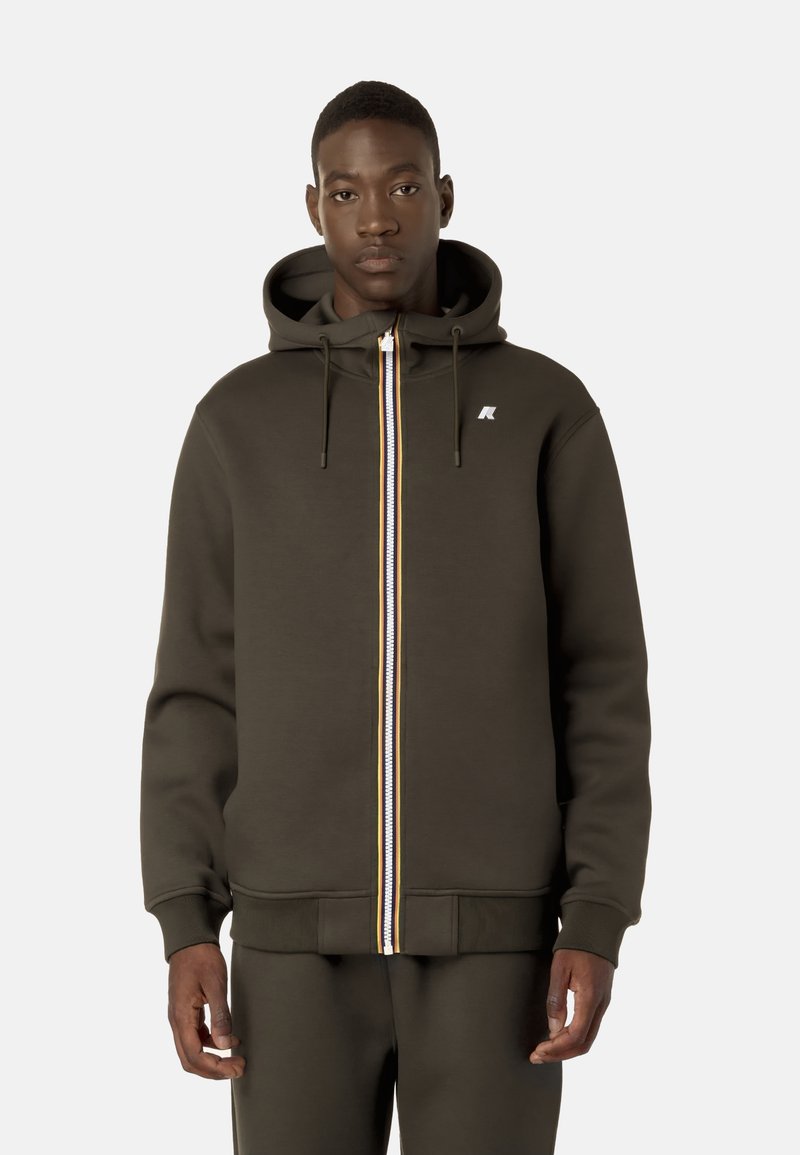 Felpa con zip di colore verde scuro, dotata di una cerniera frontale e caratterizzata da una striscia multicolore, cordini regolabili e un piccolo logo bianco sul petto.