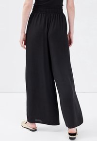 Pantalon noir à jambes larges avec taille élastique, en tissu léger, présentant une texture lisse et une silhouette fluide.