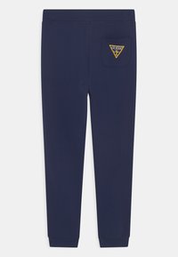 Granatowe dresy wykonane z miękkiej mieszanki bawełny, z trójkątną naszywką na tylnej kieszeni oraz elastycznymi mankietami na kostkach.