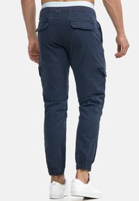 Joggers de carga en color navy con puños y cintura elásticos. Cuenta con dos bolsillos laterales y dos bolsillos traseros con solapa para almacenamiento. Material de mezcla de algodón.