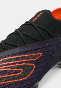 Black soccer shoe with textured upper, orange accents, and laces. Design features a distinct purple gradient at the sole with logo detail.