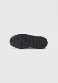Suela de zapato de goma negra con superficie texturada, que presenta surcos horizontales y un logo sutil. Bordes suaves y diseño de puntera redondeada.
