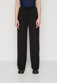 Un pantalon noir taille haute avec des jambes larges, doté d'une taille élastique et d'une texture lisse. Porté avec un haut bleu foncé et des chaussures noires.