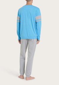 Camicia a maniche lunghe blu chiaro con strisce grigie sulle maniche, abbinata a pantaloni grigi. Il tessuto appare morbido con una vestibilità rilassata.