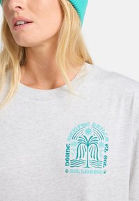 Harmaa, ylisuuri crewneck-t-paita, jossa on turkoosi palmupuugrafiikka rinnassa. Kangas näyttää pehmeältä ja siinä on kevyt rakenne.