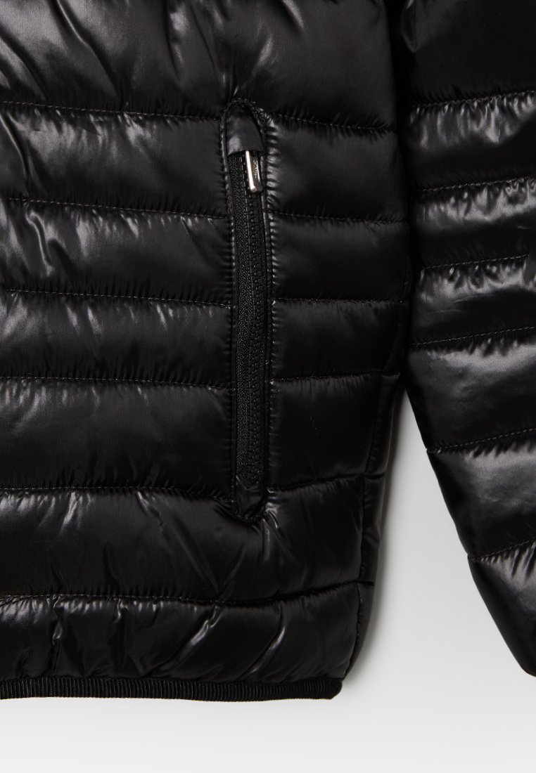 Veste matelassée noire avec un design cousu, une texture brillante, une poche zippée et un ourlet côtelé en bas.