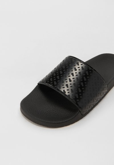 Sandale noire à glissière avec une sangle texturée présentant un motif géométrique. La semelle est en caoutchouc avec une surface texturée pour une meilleure adhérence.