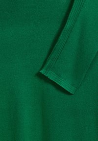 Tissu de pull en tricot vert avec une texture lisse. Gros plan sur une manche montrant un poignet côtelé et des coutures régulières.