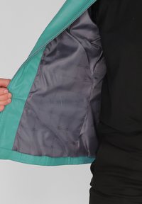 Turquoise leren jas met een grijze satijnen voering, met een ritssluiting en een interieurpatroon. Close-up van de open ritssluiting aan de binnenkant.