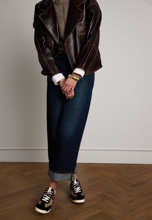 Brown leather jacket with structured design, beige sweater, wide dark denim pants, and black sneakers with leopard print accents.