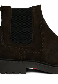 Stivale Chelsea in suede marrone con pannello laterale elastico nero, suola in gomma, cuciture visibili e un piccolo accento rosso, bianco e blu sulla suola.