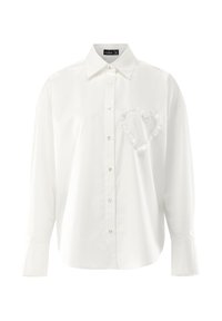 White button-up shirt made of smooth fabric featuring a heart-shaped ruffled detail on the left chest and long sleeves with buttoned cuffs.