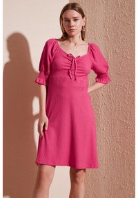 Short pink dress with puffed sleeves, a square neckline, and a tie detail at the front. Textured fabric with a slightly flared silhouette.