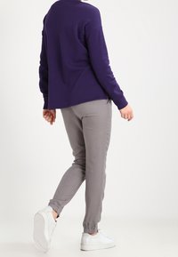 Una blusa de manga larga morada combinada con pantalones tapered grises claros, que cuentan con puños elásticos y zapatillas blancas con suelas texturizadas.