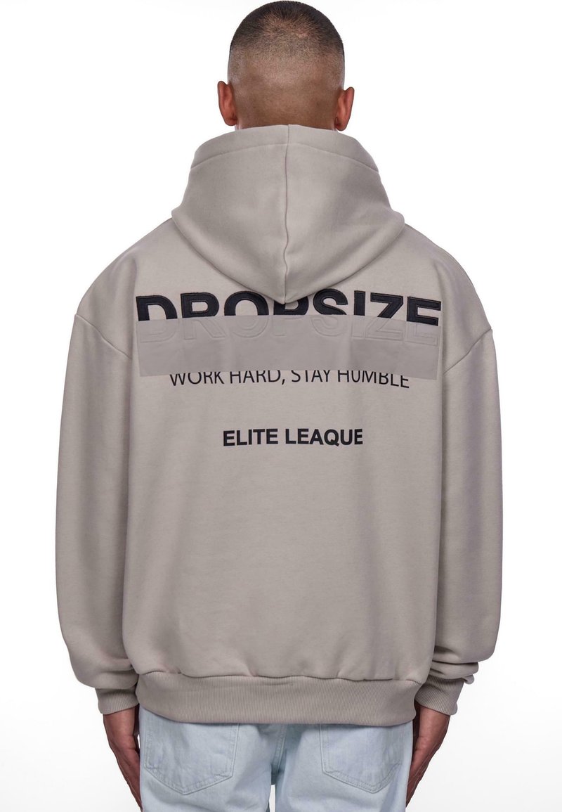 Sweat à capuche beige avec un grand logo noir « DROPSIZE » dans le dos, accompagné des inscriptions « WORK HARD, STAY HUMBLE » et « ELITE LEAGUE » en plus petit.