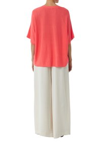 Koronkowy luźny top z krótkimi rękawami i bocznymi rozcięciami, zestawiony z białymi spodniami o szerokich nogawkach z teksturowanym wzorem.