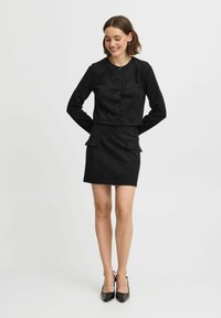Schwarze Wildleder-Cropped-Jacke mit rundem Ausschnitt und fünf Knöpfen, kombiniert mit einem passenden schwarzen Minirock mit zwei Vorderaschen.