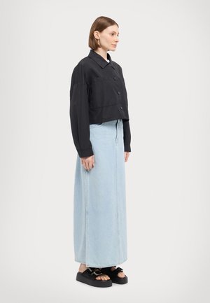Veste noire croppée à boutons et col, associée à une jupe maxi en denim bleu clair et des sandales à plateforme noires. Texture lisse sur l'ensemble.